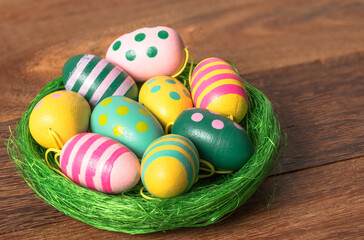 Close up of small painted wooden easter eggs on a green nest lying on a table. Eater decorations. Selective focus.
