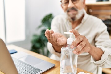 Senior grey-haired man using sanitizer hand gel working at office