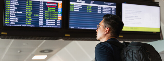 Horizontal banner or header young man reading the flights times at information departures board at the airport.
