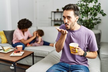 Hispanic father of interracial family drinking a cup coffee looking at the camera blowing a kiss with hand on air being lovely and sexy. love expression.