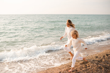Mother and young daughter running on seashore during daytime