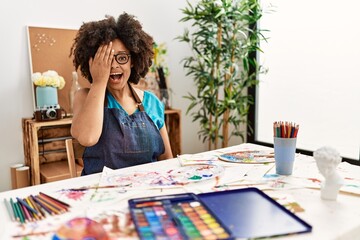 Beautiful african american woman with afro hair painting at art studio covering one eye with hand, confident smile on face and surprise emotion.