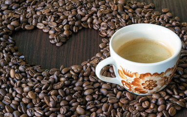 A cup of coffee surrounded by coffee beans in which the heart is made