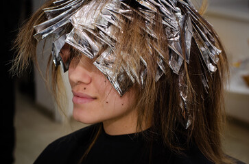 Beautiful young woman with foil on her hair. Bleaching or dyeing process. Beauty salon, fashionable...