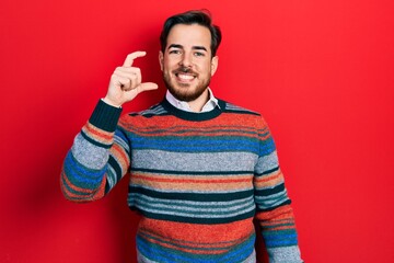 Handsome caucasian man with beard wearing elegant wool winter sweater smiling and confident gesturing with hand doing small size sign with fingers looking and the camera. measure concept.