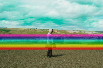 Side view of young man in pink hoodie standing on plateau outdoor with graphic strip of rainbow
