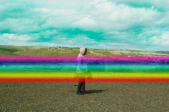 Side view of young man in pink hoodie standing on plateau outdoor with graphic strip of rainbow