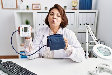 Middle age hispanic doctor woman using blood pressure monitor looking at the camera blowing a kiss...