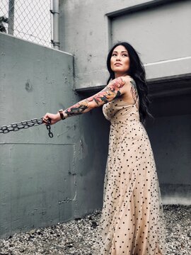 Tattooed East Asian woman in long dress holding chains