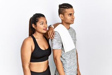 Young latin couple wearing sportswear standing over isolated background looking to side, relax profile pose with natural face with confident smile.