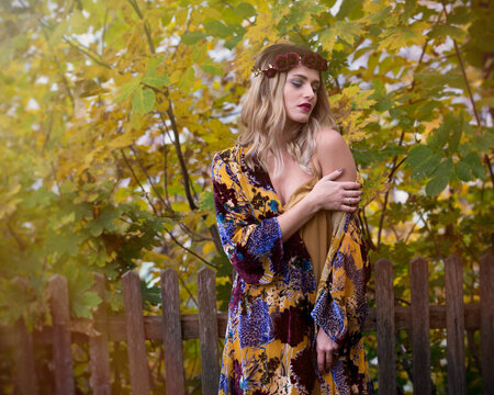 Woman in blue and yellow floral dress standing beside brown wooden fence