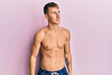 Fototapeta premium Young caucasian man wearing swimwear looking away to side with smile on face, natural expression. laughing confident.