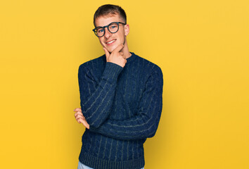 Young blond man wearing casual clothes and glasses looking confident at the camera smiling with crossed arms and hand raised on chin. thinking positive.
