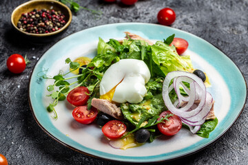 Tuna salad with poached, egg, lettuce, cherry, tomatoes olives and corn on dark stone or concrete background. Top view. copy space