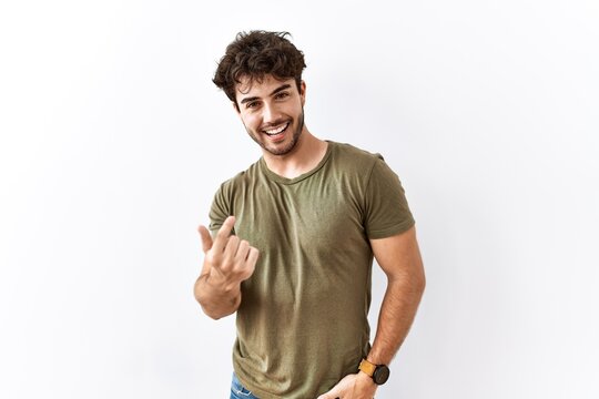 Hispanic man standing over isolated white background beckoning come here gesture with hand inviting welcoming happy and smiling