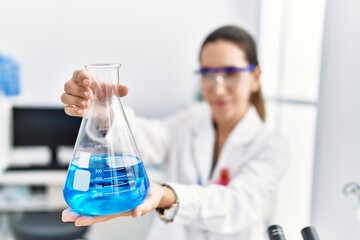 Young hispanic woman wearing scientist uniform holding test tube at laboratory