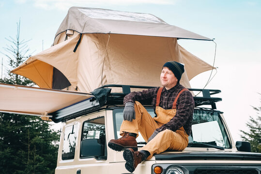 Adventurer Man Sitting Down On Roof Of The Car With Tent Mounted On It For Free Travel Camping Lifestyle