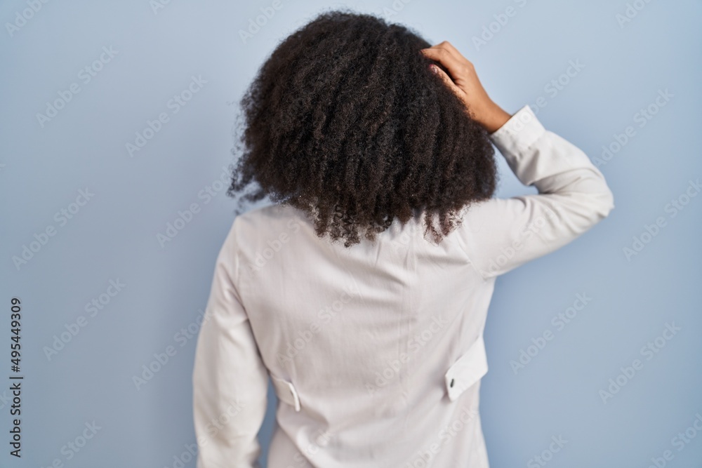 Poster Young african american woman wearing doctor uniform and stethoscope backwards thinking about doubt with hand on head