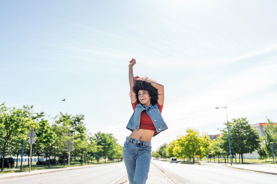 Young Black woman with Afro hair wearing denim vest with red shirt standing on the road