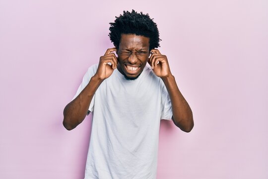 Young african american man wearing casual white t shirt covering ears with fingers with annoyed expression for the noise of loud music. deaf concept.
