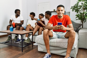 Group of african american people sitting on the sofa at home. Man smiling happy using smartphone.