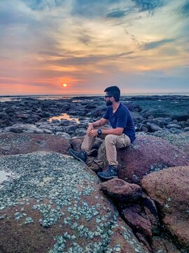 Young Man Sitting On Rock Formation At Sunset