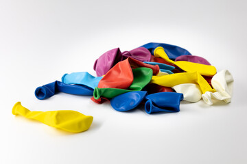 Multi-colored uninflated balloons lie in a pile on a white background isolated