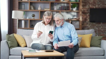 senior family couple, gray haired older pay, services enter data documents using application mobile smartphone credit card. Retirees elderly at home. utility bills, checks use computer smart phone - Powered by Adobe