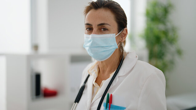 Middle age hispanic woman wearing doctor uniform and medical mask at clinic