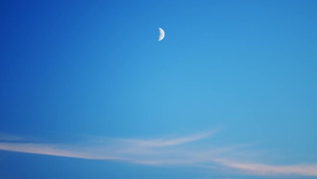 Waxing crescent half moon moving over clear blue sky background in evening.
