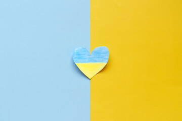 Top view of man hands holding Ukraine flag painted heart isolated on yellow, blue background. Concept symbol of help, support and no war in Ukraine
