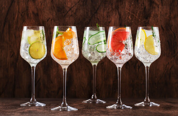 Gin and tonic cocktails set. Alcoholic drinks with lime, lemon, grapefruit, cucumber, soda and spicy herbs in wine glasses, wooden background. Summer cocktail party