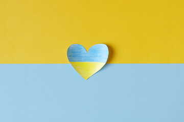 Top view of man hands holding Ukraine flag painted heart isolated on yellow, blue background. Concept symbol of help, support and no war in Ukraine