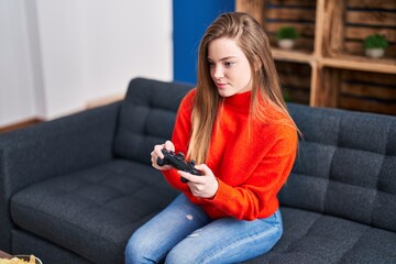 Young blonde woman playing video game sitting on sofa at home