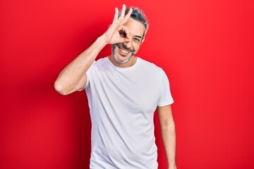 Handsome middle age man with grey hair wearing casual white t shirt smiling happy doing ok sign with hand on eye looking through fingers