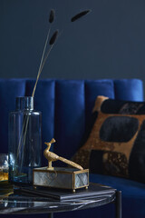 Fototapeta na wymiar Stylish close up on the elegant details in the glamour living room interior. Golden peacock and creative personal accesories. Dark blue wall. Template. Copy space..