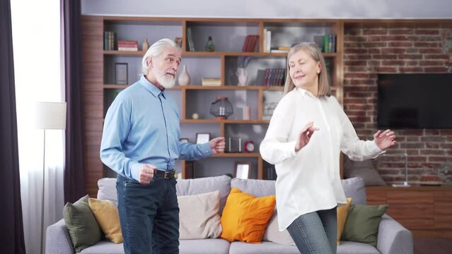 Happy Cheerful Senior Married Couple Having Fun At Home. Older Family Is Dancing. Gray Haired Retirees Rejoice Moving Active Lifestyle. Old Man And Woman Spend Leisure Time Indoors Listen To Music