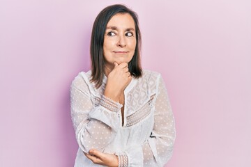 Fototapeta premium Middle age hispanic woman wearing casual clothes with hand on chin thinking about question, pensive expression. smiling with thoughtful face. doubt concept.