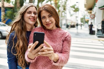 Fototapeta premium Mother and daughter hugging each other and using smartphone at street