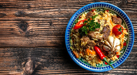 Traditional uzbek meal called pilaf. Rice with meat on plate with oriental ornament on a dark wooden background, Long banner format. space for text