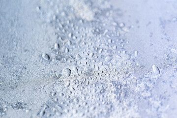 Beautiful texture of ice crystals and frozen water droplets on the glass. Winter silver-blue light background