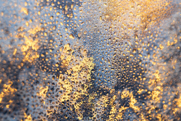 Golden texture of frozen water droplets and ice crystals close-up. Winter ice on the glass surface