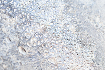 Beautiful blurred texture of ice crystals and frozen water droplets on the glass. Winter cold macro background.