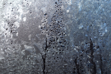 The texture of ice crystals and frozen water droplets on the window. Winter dark blue background