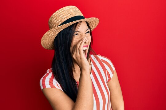 Young latin woman wearing summer hat shouting and screaming loud to side with hand on mouth. communication concept.