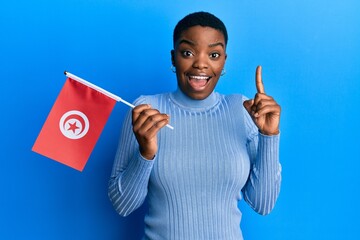 Young african american woman holding tunisia flag smiling with an idea or question pointing finger...