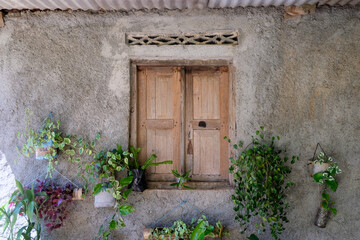 A beautiful old vintage window with closed wooden shutters,  surrounded by plants on a stone, rough textured house in rural countryside