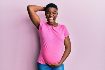 Young african american woman expecting a baby, touching pregnant belly crazy and scared with hands...