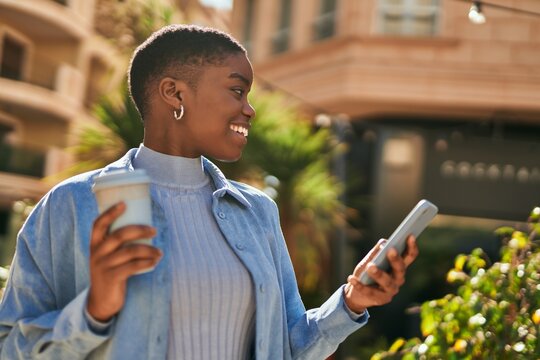 Young african american woman using smartphone and drinking coffee at the city