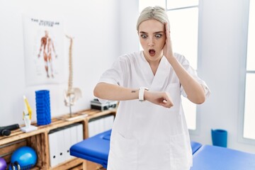 Young caucasian woman working at pain recovery clinic looking at the watch time worried, afraid of getting late
